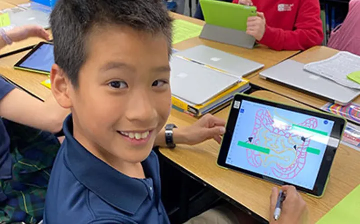 A Del Mar Pines student sits at a desk using a tablet to color a diagram